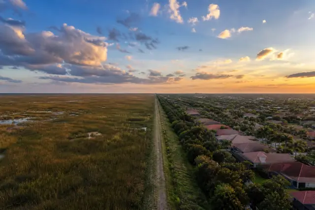 Coral Springs rooftops and palms meeting the open Everglades sawgrass landscape at the levee