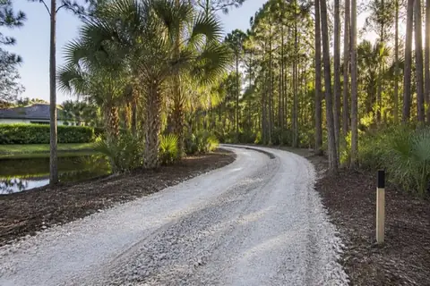 Fresh limerock two-track curving through a selectively cleared Broward acreage parcel, with mulched shoulders and cabbage palms retained in islands